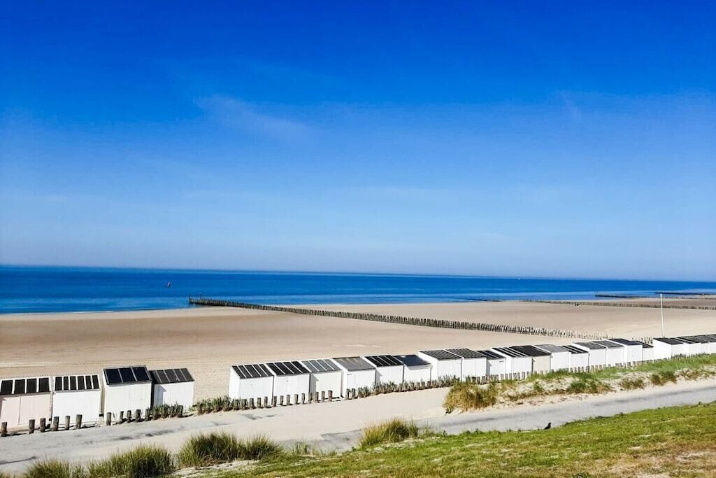 Un hotel frente al mar con una hilera de habitaciones, vista a la playa y un muelle al fondo.