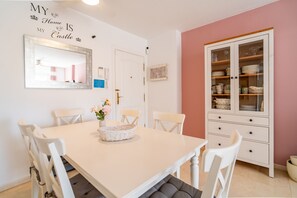 Ein Essbereich mit einem weißen Tisch, Stühlen, einer Vitrine mit Glastüren und einem Spiegel an der Wand.