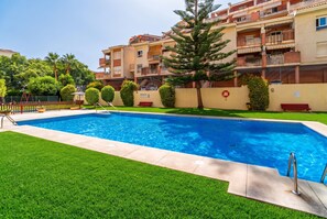 A swimming pool with a clear blue water surface, surrounded by well-maintained grass and a few trees. - Cubo's Benalmadena Apartment Pool & Parking / communal pool / air conditioning / terrace / BBQ (Benalmádena)