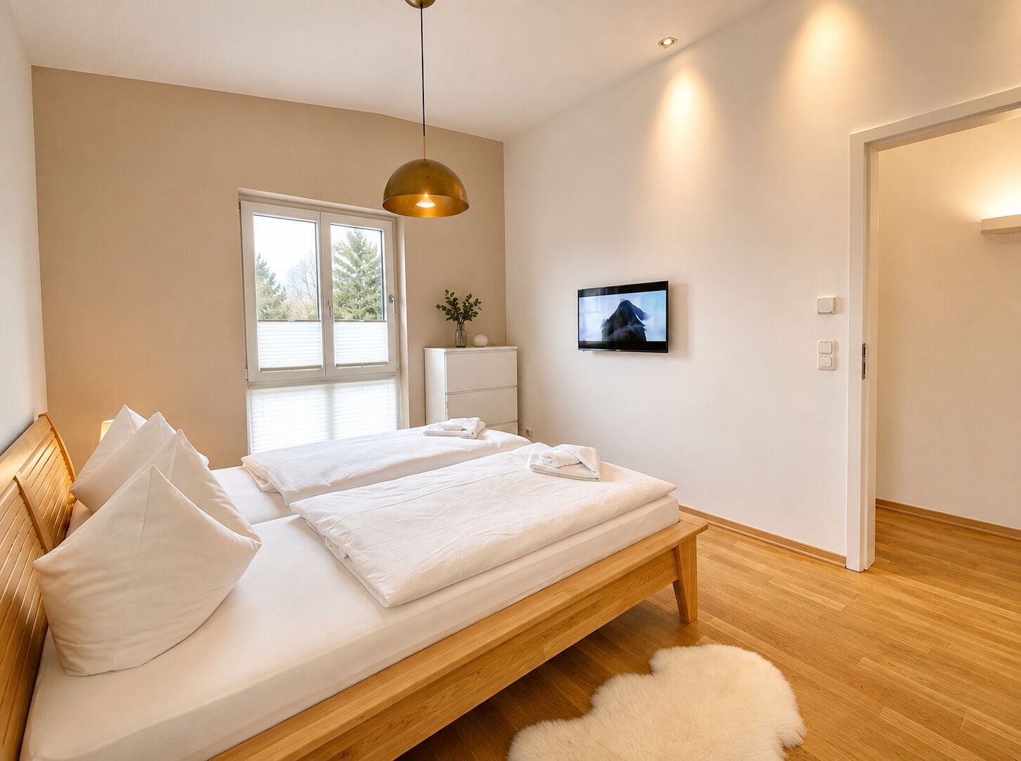 Ein modernes Schlafzimmer mit einem hölzernen Bett, einem großen Fenster, einem Fernseher und einer weißen Tür.