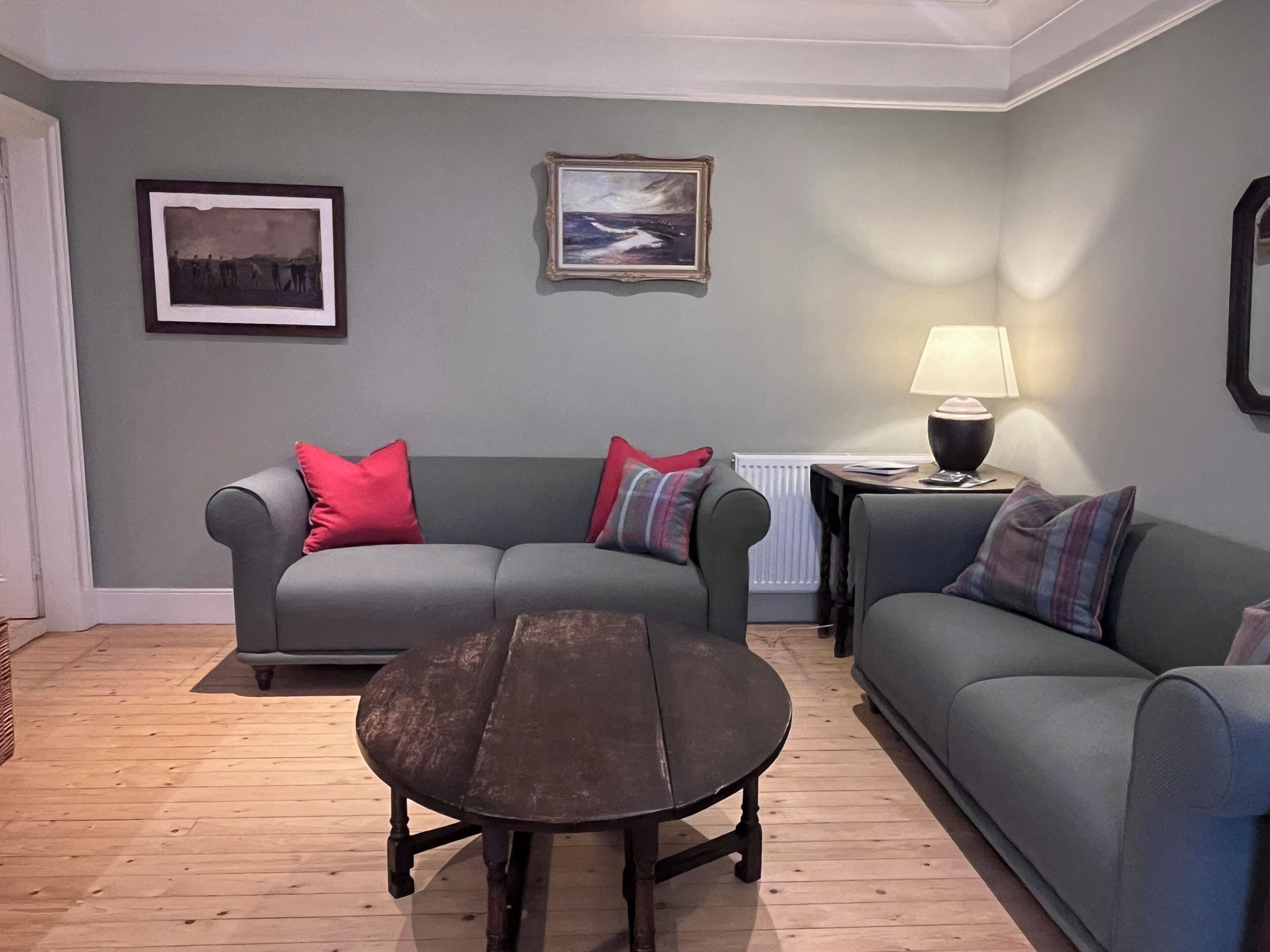 Een woonkamer met een grijze bank, een ronde salontafel en een lamp op een bijzettafeltje.