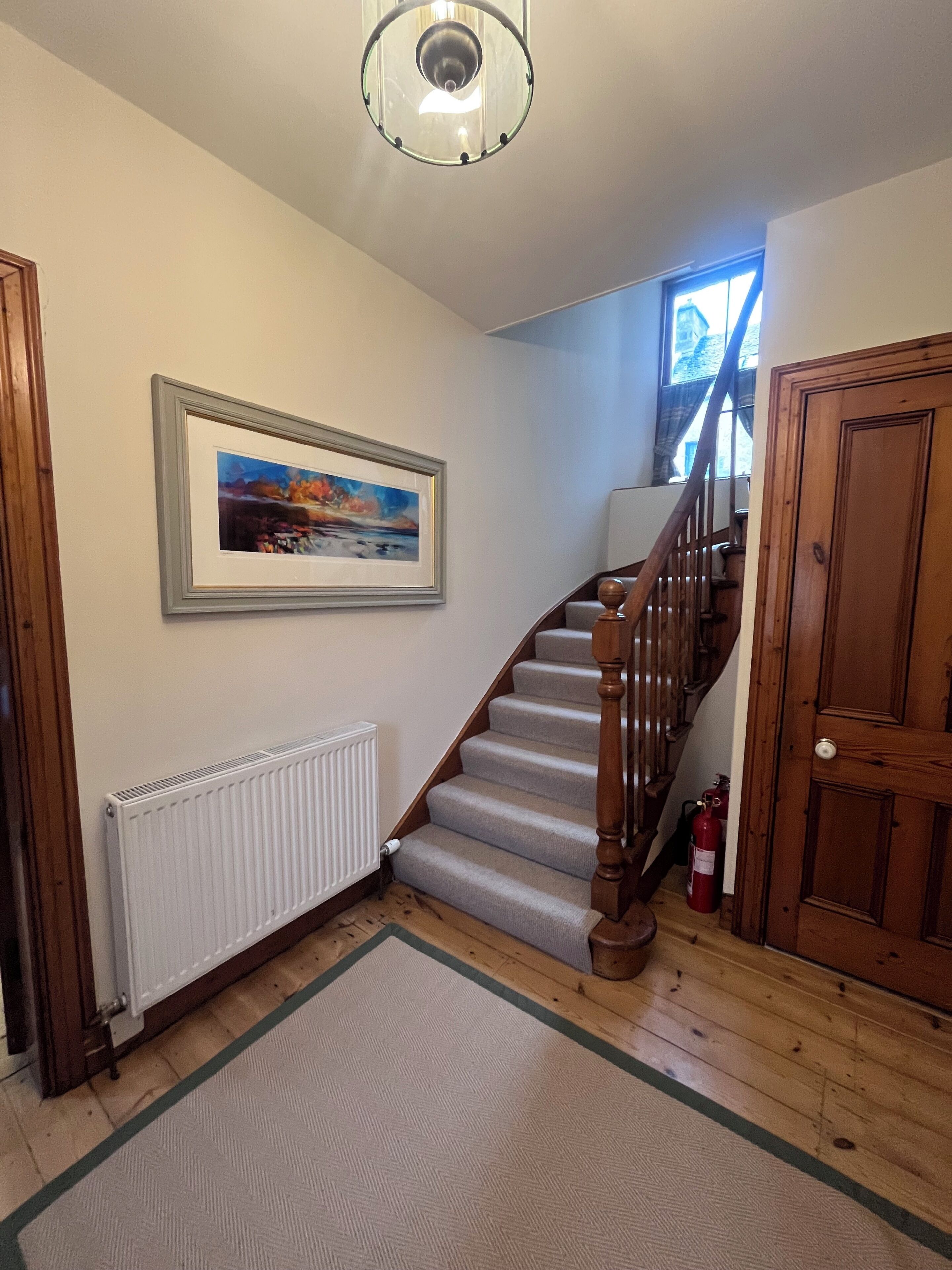 A staircase with wooden railings leading to an upper floor, a framed painting on the wall, a radiator, and a wooden door.