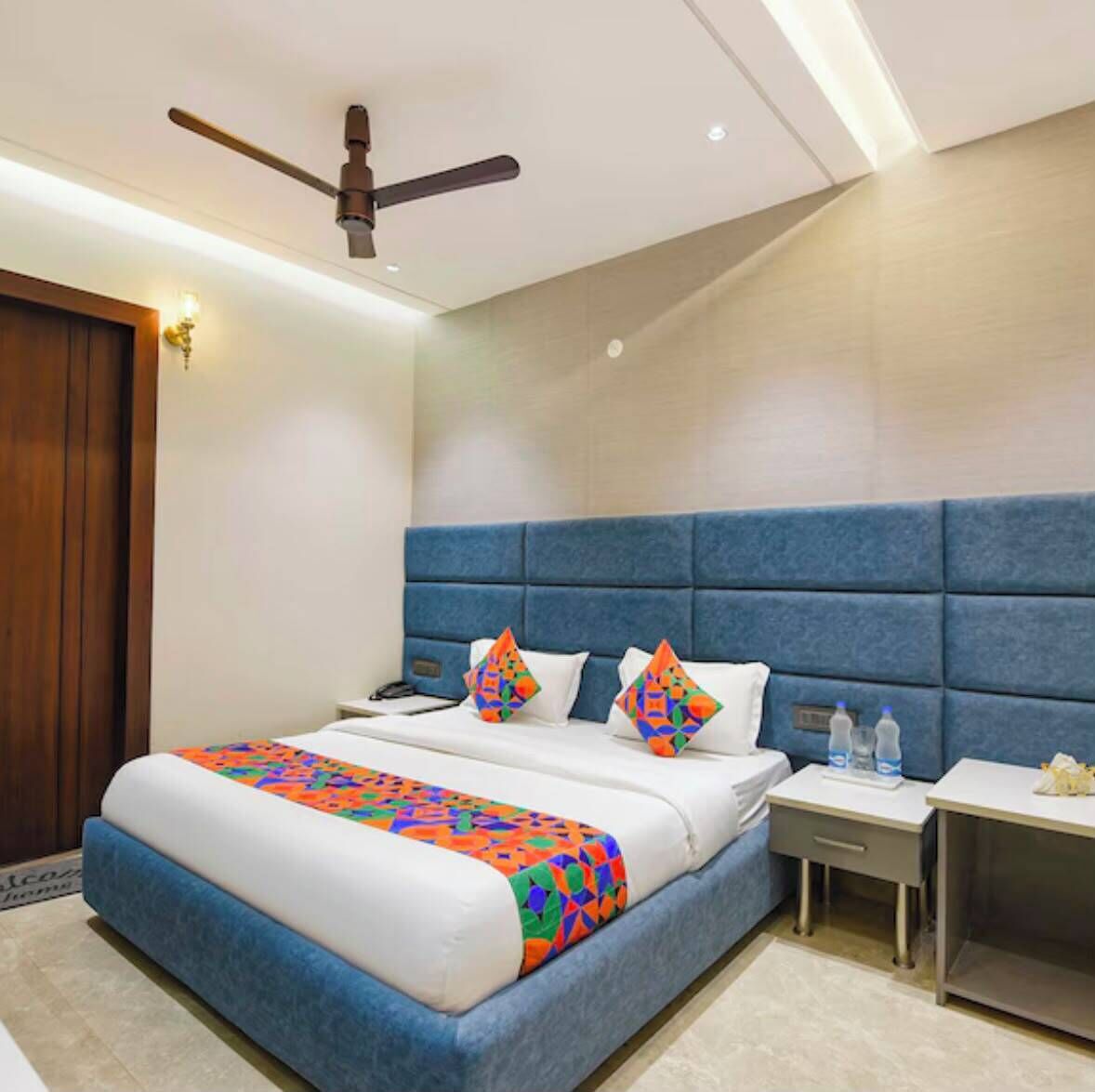 A hotel room with a bed, a nightstand, a bedside table, a ceiling fan, and a door.
