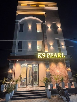 A modern building with a prominent 'K9 PEARL' sign, a glass entrance, and outdoor seating with potted plants.