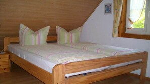 Una cama de madera con colchón y almohadas, una mesita de noche y una ventana con cortinas.