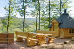 Eine Holzhütte mit Schornstein, umgeben von einer Bank und einem Picknicktisch, mit Blick auf ein bewaldetes Tal.