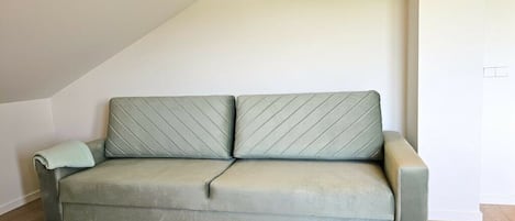 Een lichtgroene sofa met een gewatteerd patroon, geplaatst in een hoek met een houten vloer, tegen een witte muur met een airconditioner gemonteerd erboven.