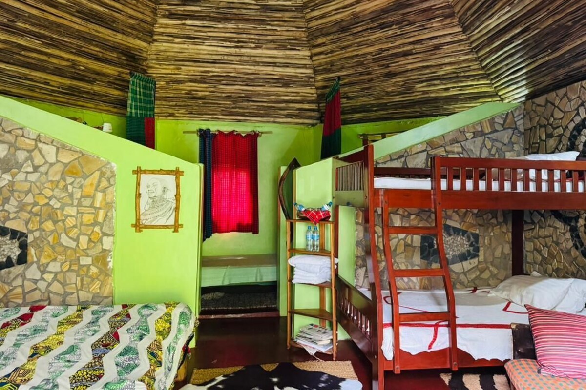 A room with bunk beds, a stone wall, a window with red curtains, and a small shelf with items.