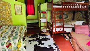 Una habitación con literas, una colcha estampada, una pared de piedra y una cortina roja.