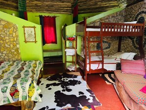 A room with bunk beds, a patterned bedspread, a stone wall, and a red curtain. - Songota Falls Retreat (Arusha)