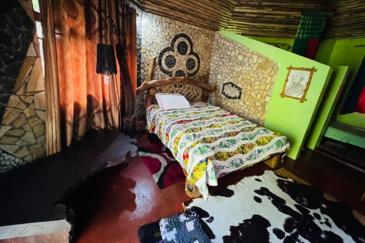 A room with a bed, a stone wall, a wooden ceiling, and a green wall with a framed picture.