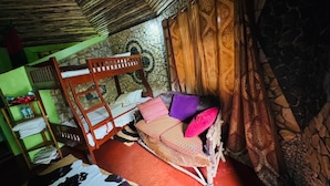 Una habitación con una cama litera, un sofá con cojines, una cortina estampada y una pared de piedra.