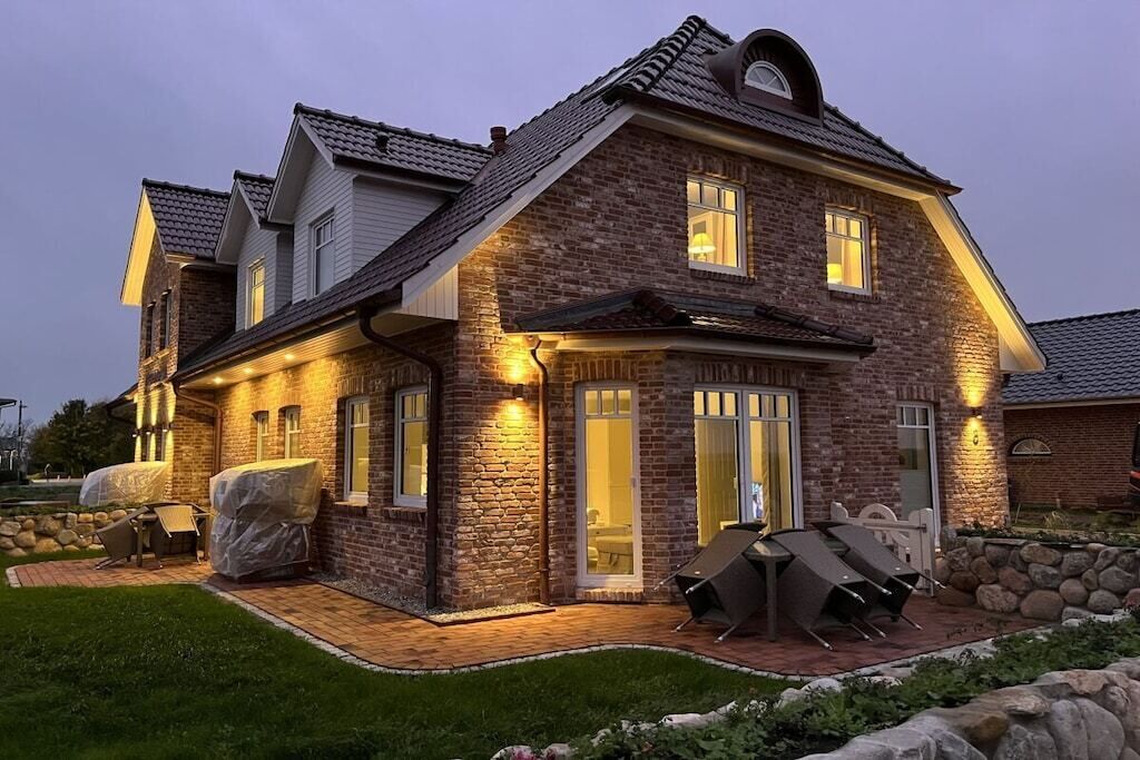 A two-story house with a brick exterior, a covered patio with outdoor furniture, and a well-lit entrance.