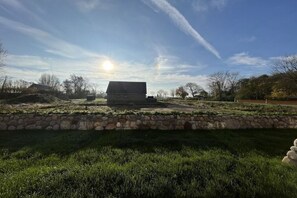 A house with a stone wall in the foreground, a clear sky, and a sun in the background. - Holiday home with 4 bedrooms (Tetenbüll)
