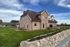 A two-story house with a stone facade, a dark roof, and a well-maintained lawn. - Holiday home with 4 bedrooms (Tetenbüll)
