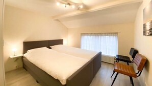 A bedroom with a bed, a chair, a nightstand, and a window with curtains. - DO19 Holiday home Domburg (Domburg)
