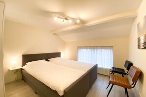 A bedroom with a bed, a chair, a nightstand, and a window with curtains. - DO19 Holiday home Domburg (Domburg)