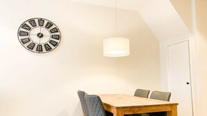 A dining area with a wooden table, four chairs, a wall clock, and a hanging light fixture. - DO19 Holiday home Domburg (Domburg)