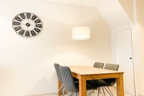 A dining area with a wooden table, four chairs, a wall clock, and a hanging light fixture. - DO19 Holiday home Domburg (Domburg)