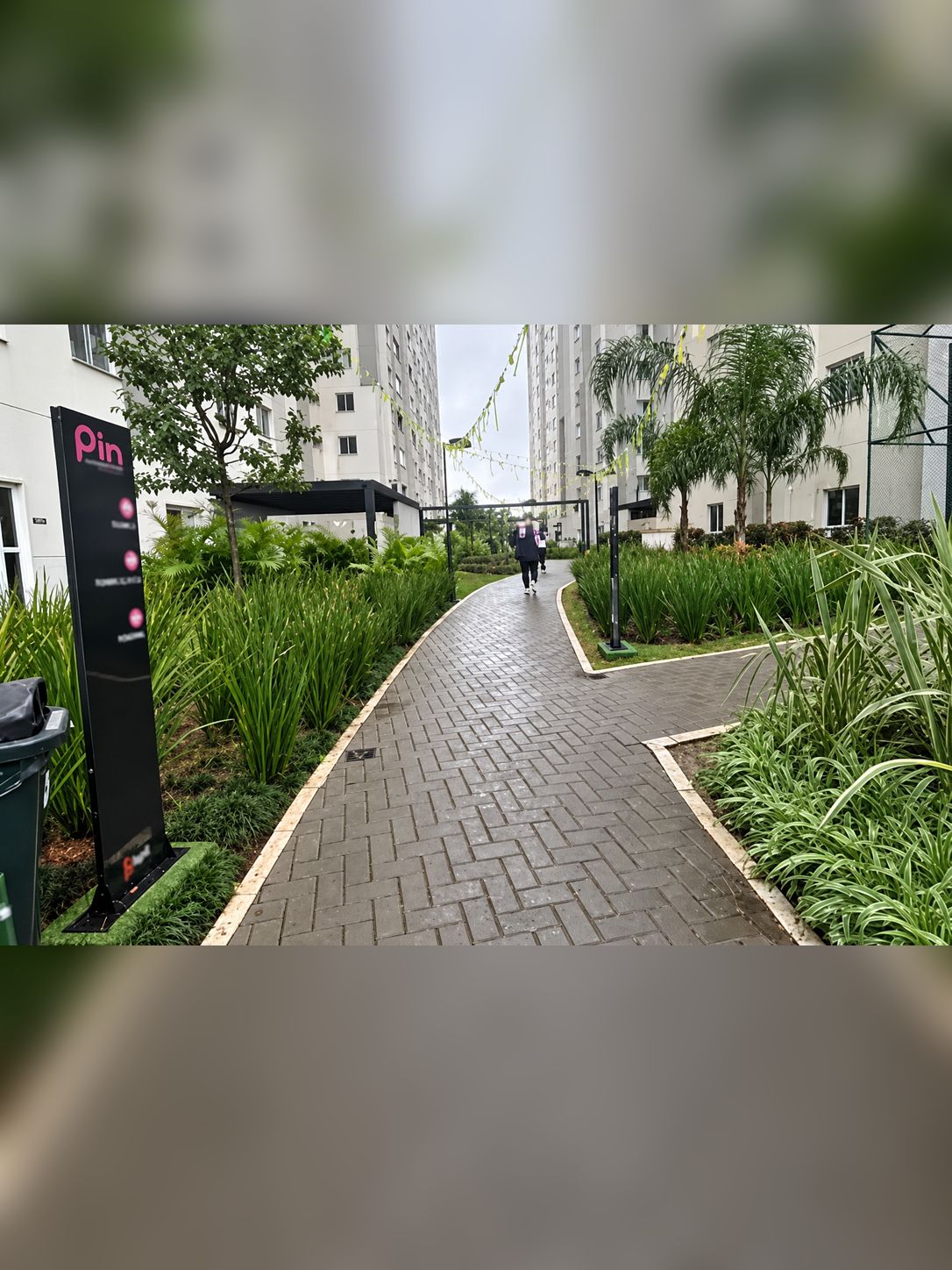 A pathway leading to a residential building with a signboard on the left.