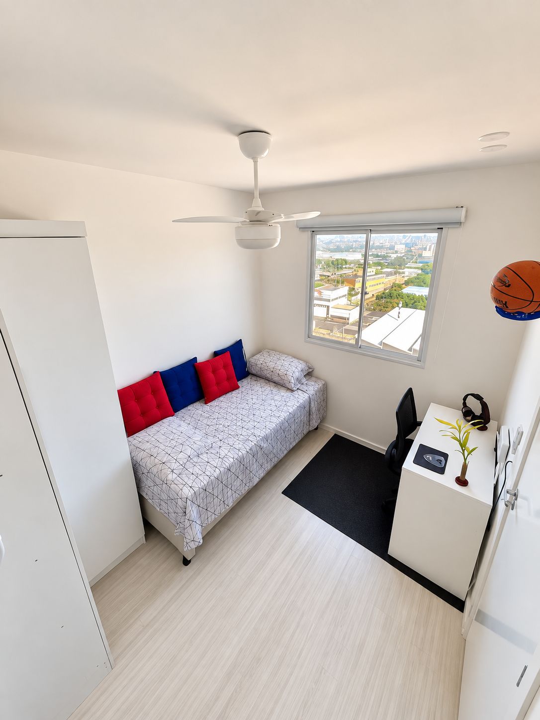 A compact bedroom with a bed, a desk, a chair, a ceiling fan, and a window with a view.