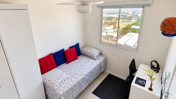 A compact bedroom with a bed, a desk, a chair, a ceiling fan, and a window with a view.