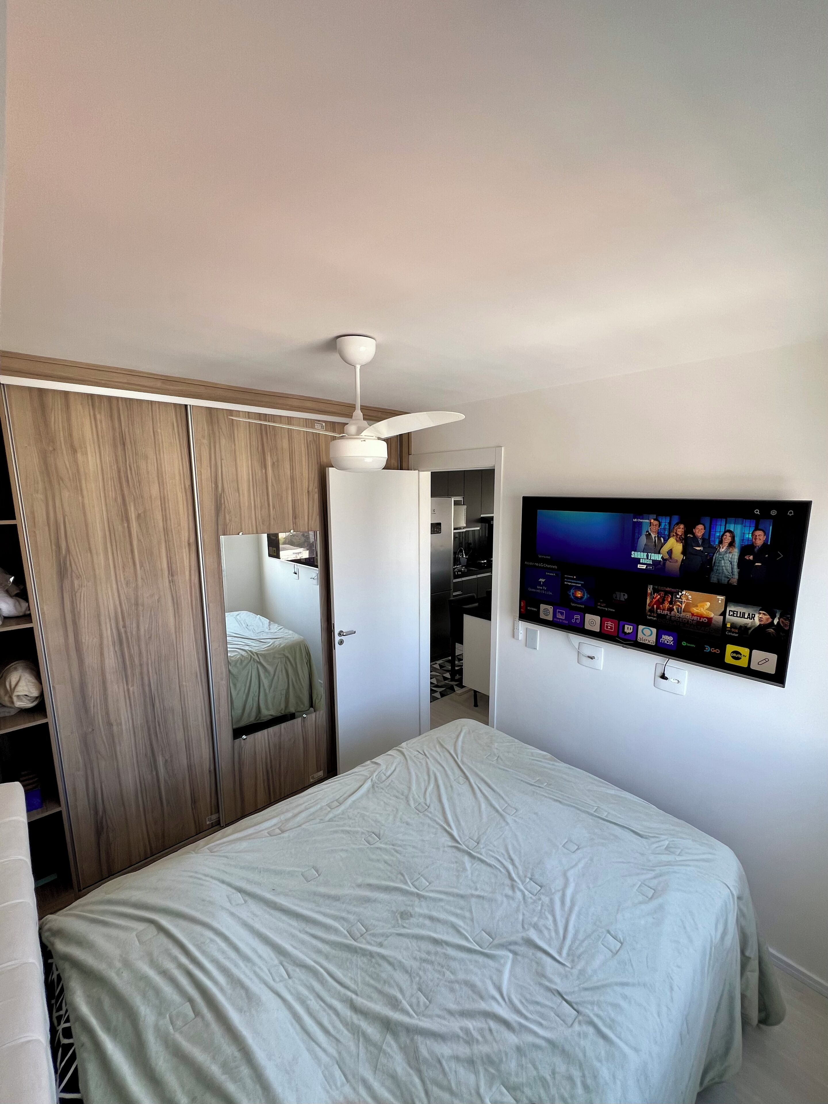 A bedroom with a bed, wardrobe, and a television mounted on the wall.