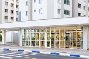 Una entrada de hotel moderna con fachada de vidrio, un paseo techado y un camino de acceso portón cerrado.