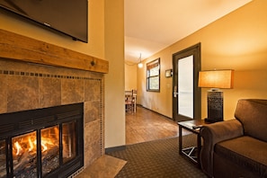 Una sala de estar con chimenea, un sofá, una lámpara y un comedor al fondo.