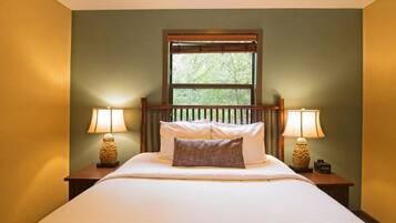 Une chambre avec un lit, deux lampes de chevet, une fenêtre avec des stores et une vue sur la verdure.