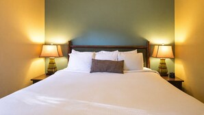 A neatly made bed with white linens and two pillows, flanked by two bedside tables with lamps, in a room with a simple, clean design. - Wisconsin Dells | Pool & Waterpark Access | 2BR Cottage (Wisconsin Dells)