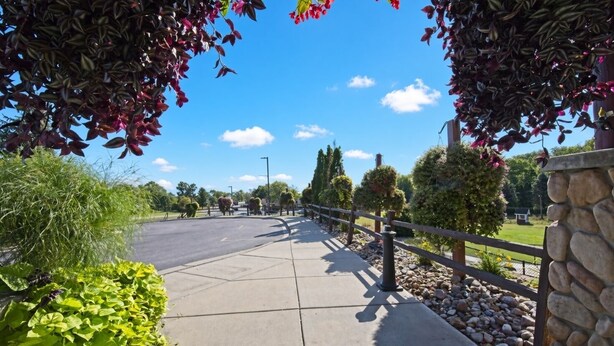 A paved walkway with a stone wall on one side and a metal fence on the other, leading to a parking area. - Wisconsin Dells | Pool & Waterpark Access | 2BR Cottage (Wisconsin Dells)