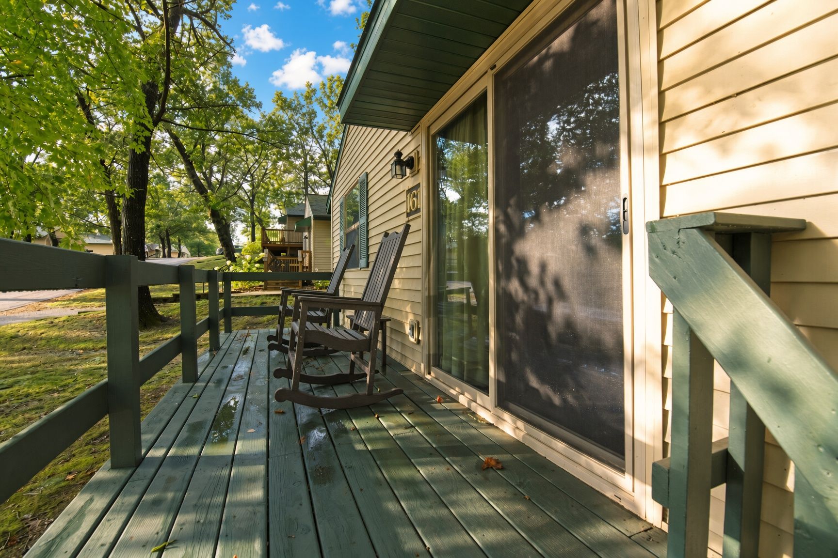 A wooden deck with rocking chairs, a covered porch, and a screened window.