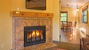 A fireplace with a TV mounted above it, a dining area with chairs and a table, and a hallway leading to another room. - Wisconsin Dells | Pool & Waterpark Access | 2BR Cottage (Wisconsin Dells)