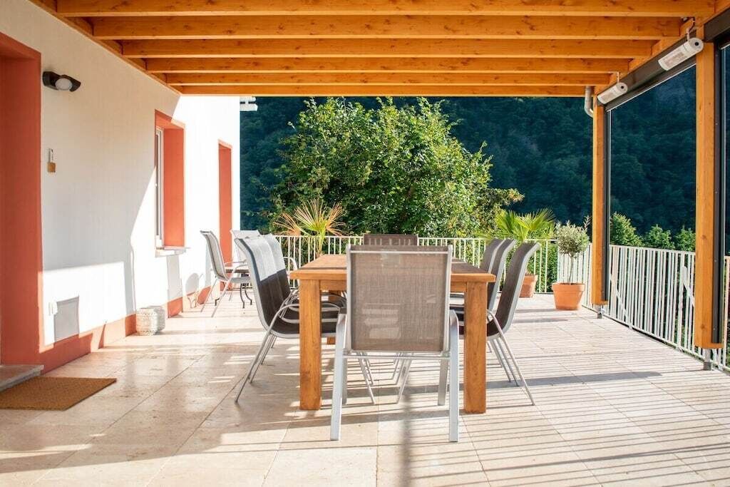 Une terrasse extérieure avec une table et des chaises en bois, entourée de plantes en pot et offrant une vue sur une zone boisée.