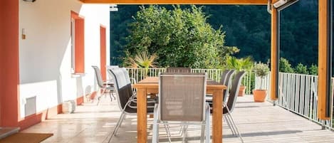 Une terrasse extérieure avec une table et des chaises en bois, entourée de plantes en pot et offrant une vue sur une zone boisée.