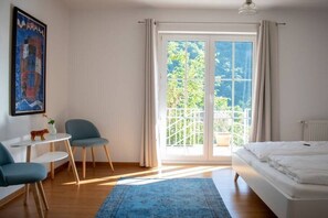 A bedroom with a bed, a desk, two chairs, a window with curtains, and a view of greenery outside. - at the Johanneshof winery (Minheim)