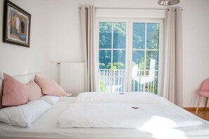 A bedroom with a large bed, a radiator, a window with curtains, and a chair. - at the Johanneshof winery (Minheim)