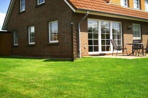 Une maison en briques avec un toit rouge, un patio couvert avec des meubles d’extérieur et une pelouse bien entretenue.