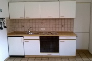 A compact kitchen with white cabinets, a sink, and a stove. - Holiday apartment with 2 bedrooms (Neßmersiel)