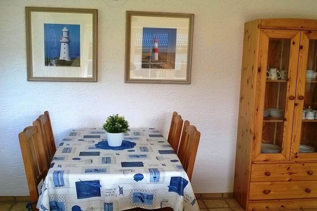 Un coin repas avec une table dressée pour quatre personnes, des tableaux encadrés au mur et un buffet en bois contenant de la vaisselle.