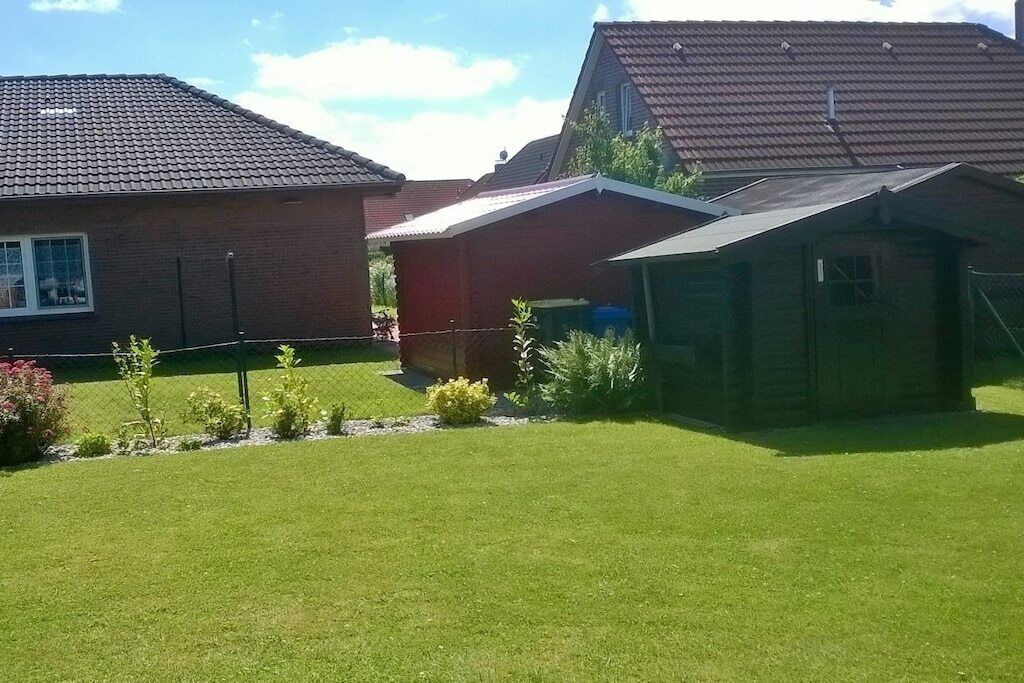 Een woonwijk met een verzorgd gazon, een rieten huis en een houten tuinhuis.