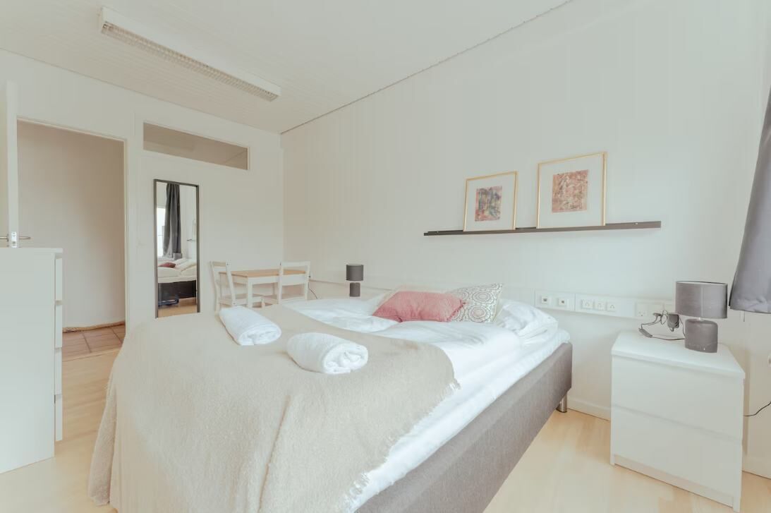 Una habitación de hotel moderna con cama, mesita de noche y un pequeño escritorio.