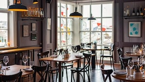 Een restaurantinterieur met meerdere eettafels, stoelen, hangende吊灯 en een uitzicht door grote ramen.