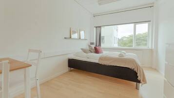 A bedroom with a bed, a chair, a window, and a shelf with pictures.