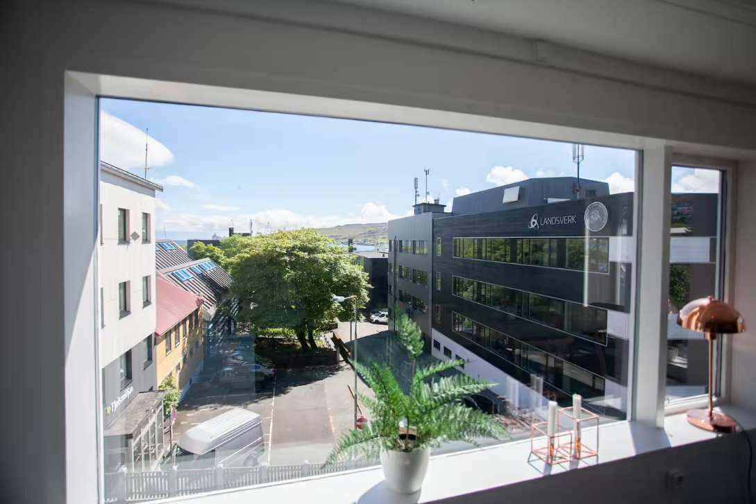 Blick aus einem Fenster auf ein modernes Gebäude mit dem Schild 'LANDSVERK' und einem wolkenlosen Himmel.