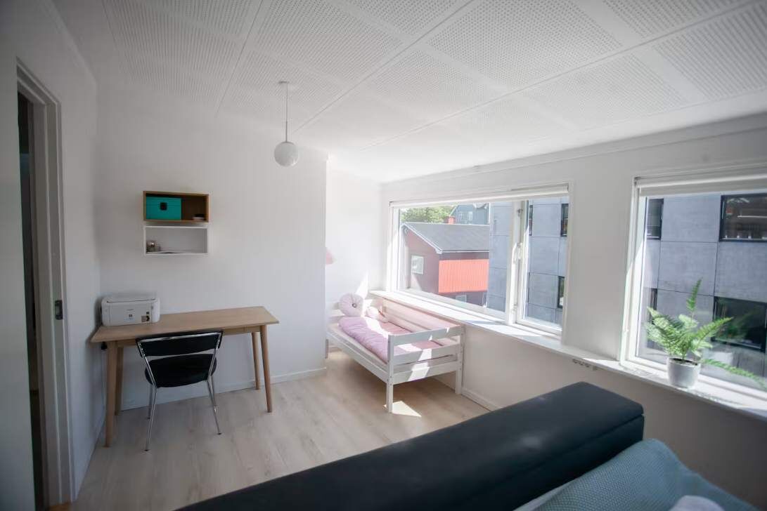 Una habitación con una cama, un escritorio, una silla, un ventanal y una planta en maceta.
