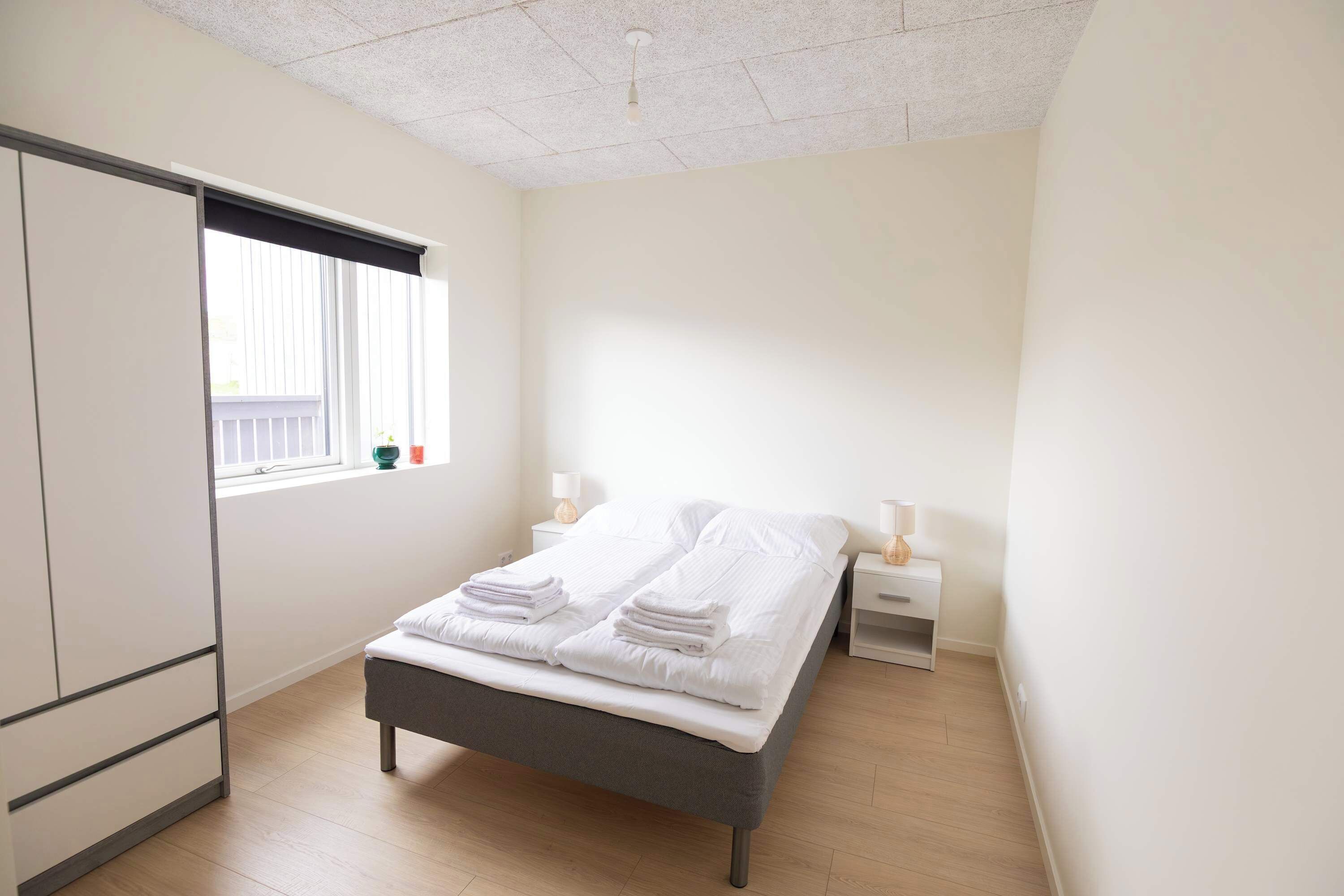 Une chambre à coucher avec un lit, des tables de chevet, une fenêtre et une armoire.