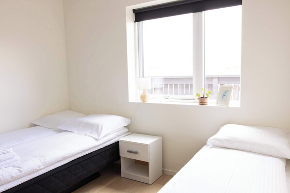 A small, bright room with two single beds, a nightstand, and a window with a view of the balcony.