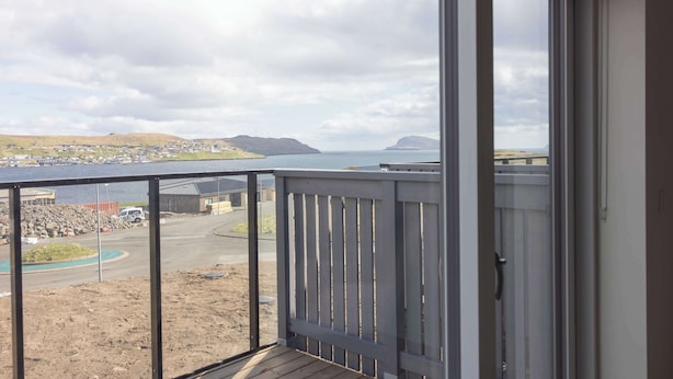 En balkon med udsigt over en kystby, en parkeringsplads og et vandområde.